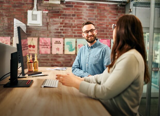 Ein Mann und eine Frau stehen an einem Holzschreibtisch in einem Büro und reden miteinander.