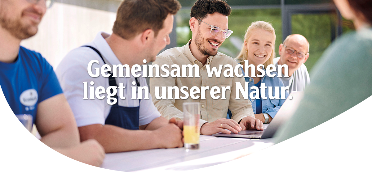 Mehrere Personen sitzen an einem Tisch vor einem Laptop und lächeln, Headline: 'Gemeinsam wachsen liegt in unserer Natur'.