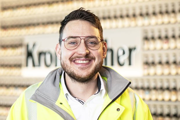 Portrait von Michael Müller, HR Business Partner. Er hat braune Haare, trägt eine Brille und eine gelbe Sicherheitsjacke mit reflektierenden Streifen mit Krombacher Logo.