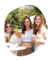 Drei junge Frauen stehen im Freien, halten Krombacher Seidel Biergläser und tragen ganz kleine Krombacher Schützenfest Hüte, eine trägt ein weißes Crop-Top und Leopardenmuster-Hose.