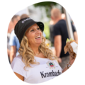 Frau mit langen blonden Haaren trägt Krombacher-Mütze und T-Shirt, hält ein Burger in der Hand