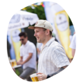 Mann mit hellbeiger Kappe und gestreiftem Hemd hält ein Glas Bier auf dem Krombacher Sommerfest